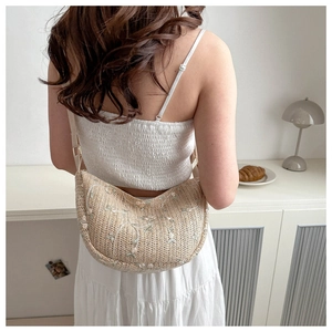 Detail of hand-woven beige straw crossbody bag featuring delicate white floral embroidery