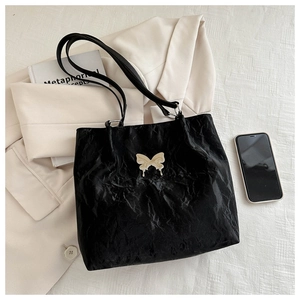 Detail of black wrinkled texture tote bag with cream butterfly logo on light fabric