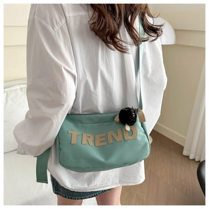 Side view of mint green oxford crossbody bag with TREND patch and black pompom charm