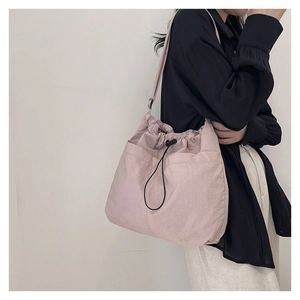Pink drawstring bucket bag with textured fabric and large front pockets shown on shoulder