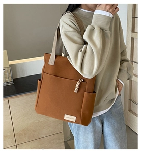 Dettaglio di una borsa tote in tela marrone con ampia tasca frontale e cerniera intrecciata
