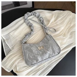Détail du sac plissé argenté avec papillon en métal et bandoulière froncée élégante