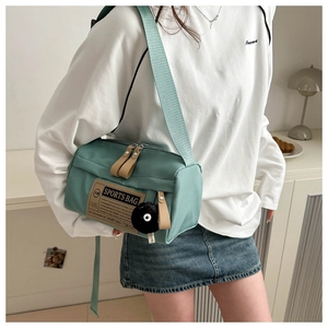 Close-up of mint green Oxford cloth crossbody bag with black pompom and sports patch