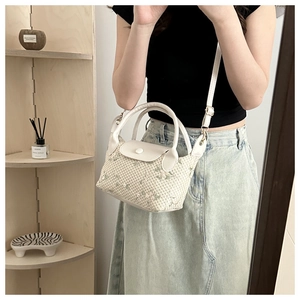 Close-up of woven cream handbag with light green floral embroidery and white leather strap