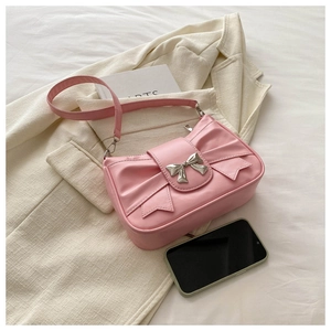 Detailed view of pink bow shoulder bag with silver metal ornament on a beige jacket
