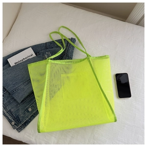 Flat lay detail of a neon green mesh beach tote bag with thin straps on a white fabric surface
