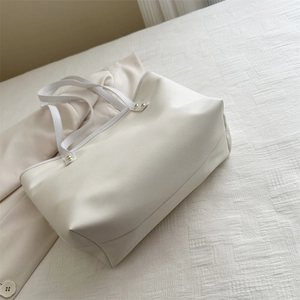 Borsa tote minimalista in pelle bianco crema con borchie dorate su superficie bianca