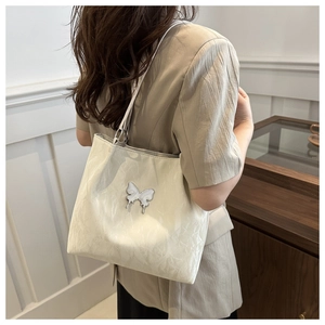 Detail of butterfly metal logo on creamy white tote bag with textured leather surface