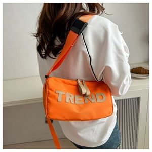 Detail of orange nylon crossbody bag showing TREND patch and adjustable wide strap