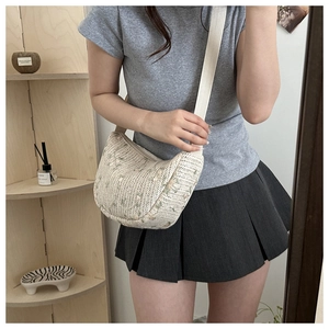 Model wearing a half-moon woven crossbody bag with green floral embroidery detail