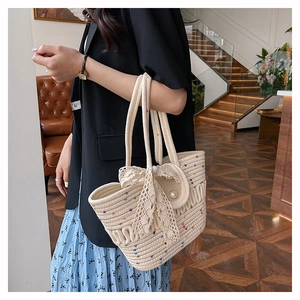 Detail of a beige woven tote bag with lace bow and pearl accents on a model