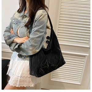 Detailed view of large black glossy hobo shoulder bag with pleated texture on model