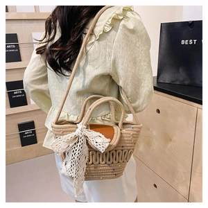 Detail of woven straw bucket bag with large white lace bow and brown leather flap