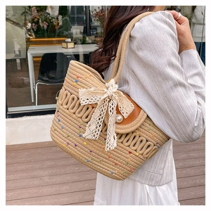 Detail of woven straw bucket bag with colorful pom-poms, lace bow, and pearl decoration