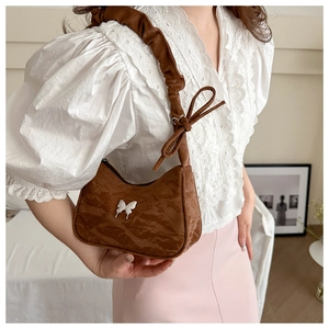 Detail of a brown pleated shoulder bag featuring a white metal butterfly buckle and bow strap