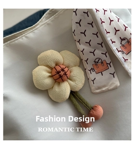 Detail of a beige fabric flower charm with orange center and woven green cords on a tote bag