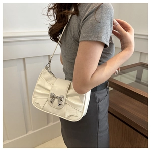 Close-up of white leather bow shoulder bag with silver metallic clasp on a model