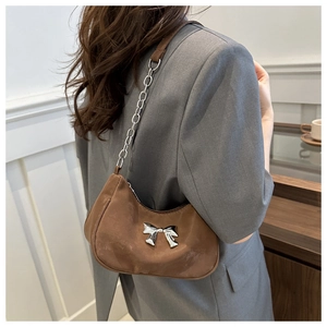 Detail of a brown suede underarm bag with a silver metal bow and chain strap on a blazer