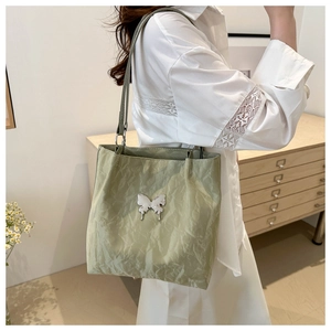Close-up of light green tote bag with silver butterfly charm and crinkled finish texture