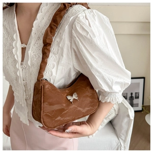 Détail d'un sac à bandoulière en cuir plissé marron avec ornement papillon en métal argenté