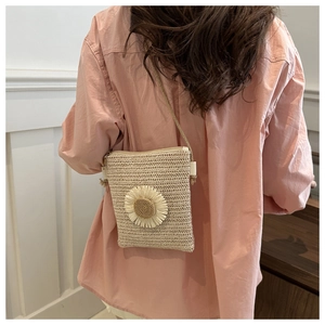 Detail of a beige woven straw crossbody bag with a white daisy floral decoration