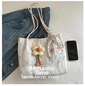 Detail of white jacquard tote bag with floral pendant and silk scarf on handle