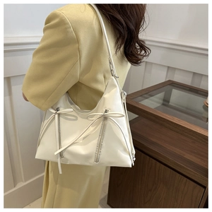Detail of white faux leather tote with ribbon bow and zipper on a yellow blazer