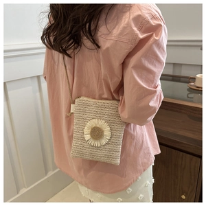 Detail of a beige woven straw crossbody bag featuring a large decorative 3D daisy flower