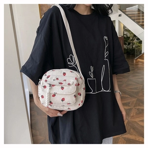 Detail of off-white corduroy round crossbody bag with strawberry embroidery worn by a model