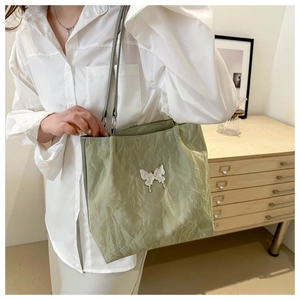 Detail of light green pleated tote bag featuring a metallic silver butterfly badge
