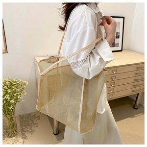 Side view of beige mesh tote bag worn by model in minimalist indoor home setting