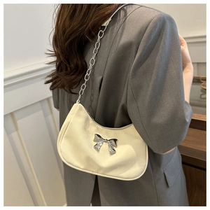 Detail of a creamy beige underarm bag with silver bow accent and metal chain strap