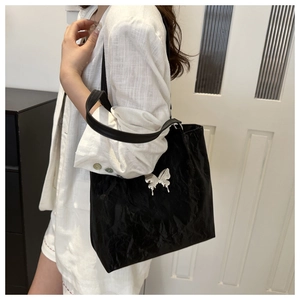 Detail of glossy black tote bag with silver butterfly emblem on a model in white suit