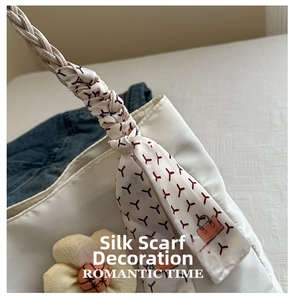 Detail of cream fabric handbag featuring a floral charm and silk scarf wrapped handle