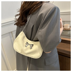 Detail of cream white underarm bag featuring a silver bow and chunky chain strap