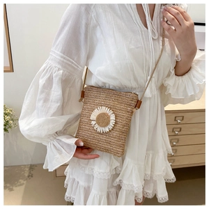 Straw square crossbody bag with daisy detail worn over a white lace dress in a cozy setting