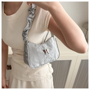 Détail d'un sac à bandoulière argenté métallisé avec texture plissée et papillon en métal