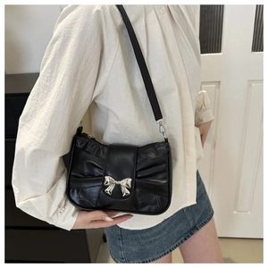 Detail of a black handbag with silver metal bow buckle and elegant pleated side details
