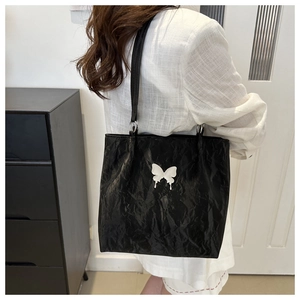 Detail of black pleated leather tote bag with white butterfly patch on shoulder model