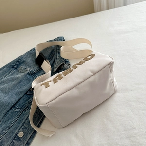 Off-white Oxford cloth crossbody bag with TREND applique on white textured bedsheet