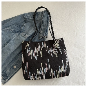 Detail of black quilted tote bag with colorful embroidery and woven handles on fabric
