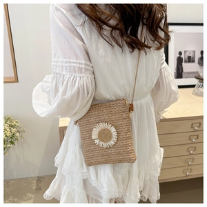 Detail of a woven straw crossbody bag with white daisy flower and thin shoulder strap