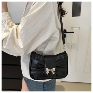 Detail of black faux leather handbag featuring large bow folds and a silver metal buckle
