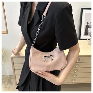 Pink underarm bag with metal bow detail and silver chain strap worn by a model