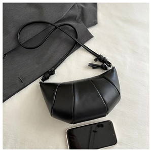 Detail of black pleated croissant bag with knotted strap next to a smartphone for scale