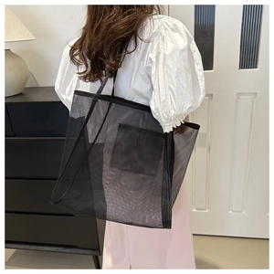 Detail of a large black mesh tote bag with reinforced handles and interior pocket for travel