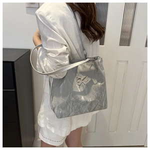 Détail du sac cabas argenté plissé avec breloque papillon porté à l'épaule par un mannequin