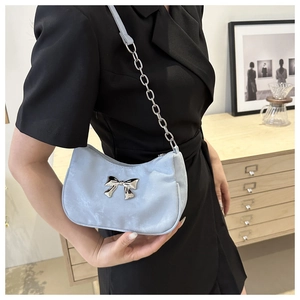 Close-up of light blue satin underarm bag featuring a silver metal bow and chain strap