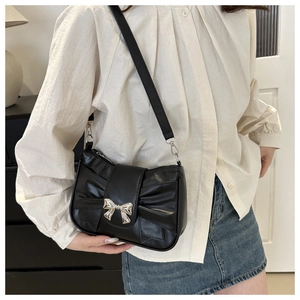 Close-up of black leather bow bag with silver metallic buckle and gathered texture