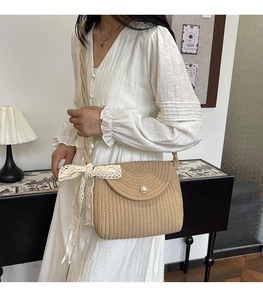 Detailed close-up of woven straw bag with large pearl buckle and delicate lace bow